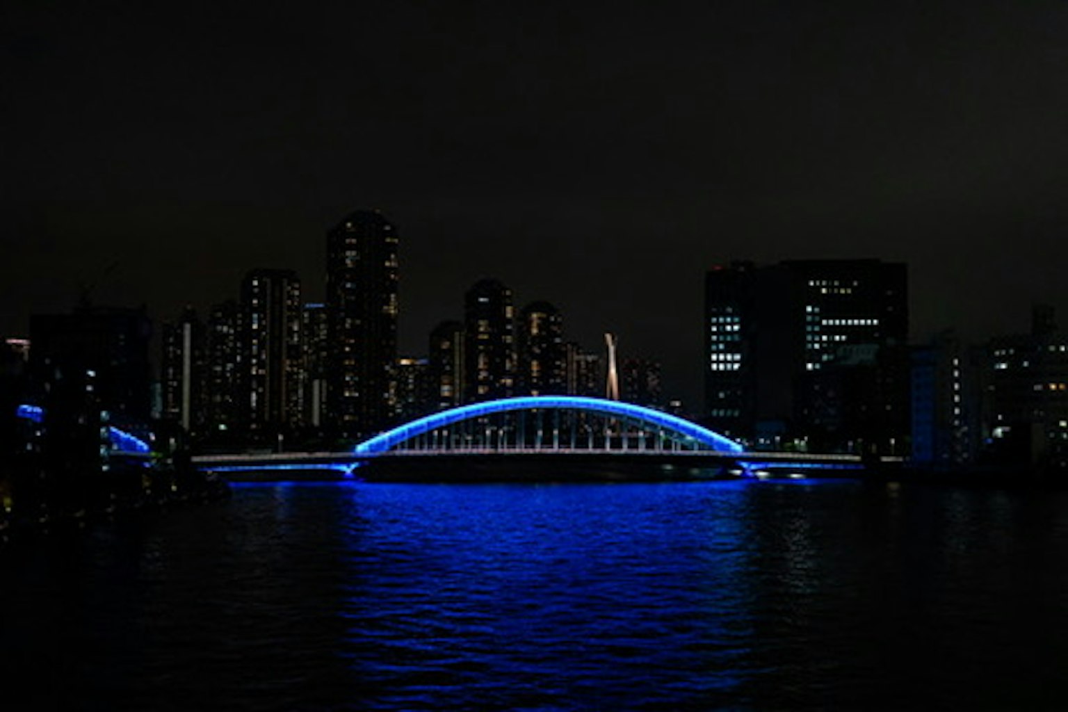Puente arqueado azul iluminado contra un horizonte urbano de noche