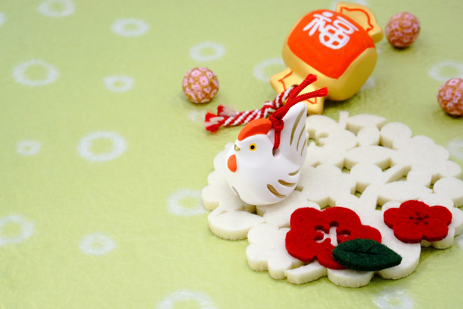 Una galleta blanca con decoraciones de flores rojas y una figurita de pájaro blanco sobre un fondo verde junto a un amuleto con el carácter de fortuna
