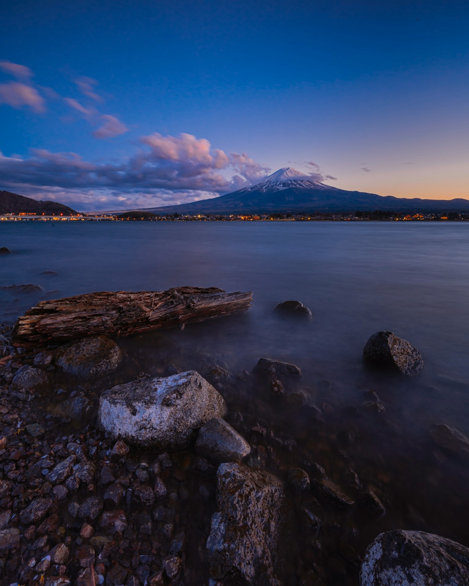 Paesaggio di riva al lago con cielo blu e nuvole Montagna sullo sfondo con rocce e legno di deriva in primo piano
