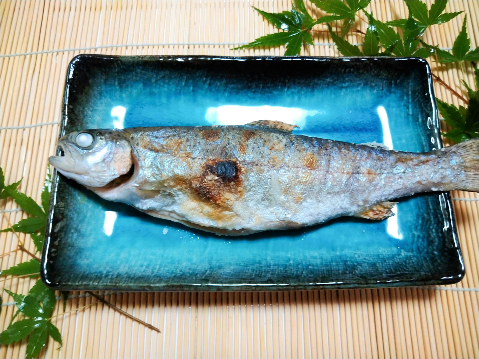 Pesce grigliato su un piatto blu circondato da foglie verdi