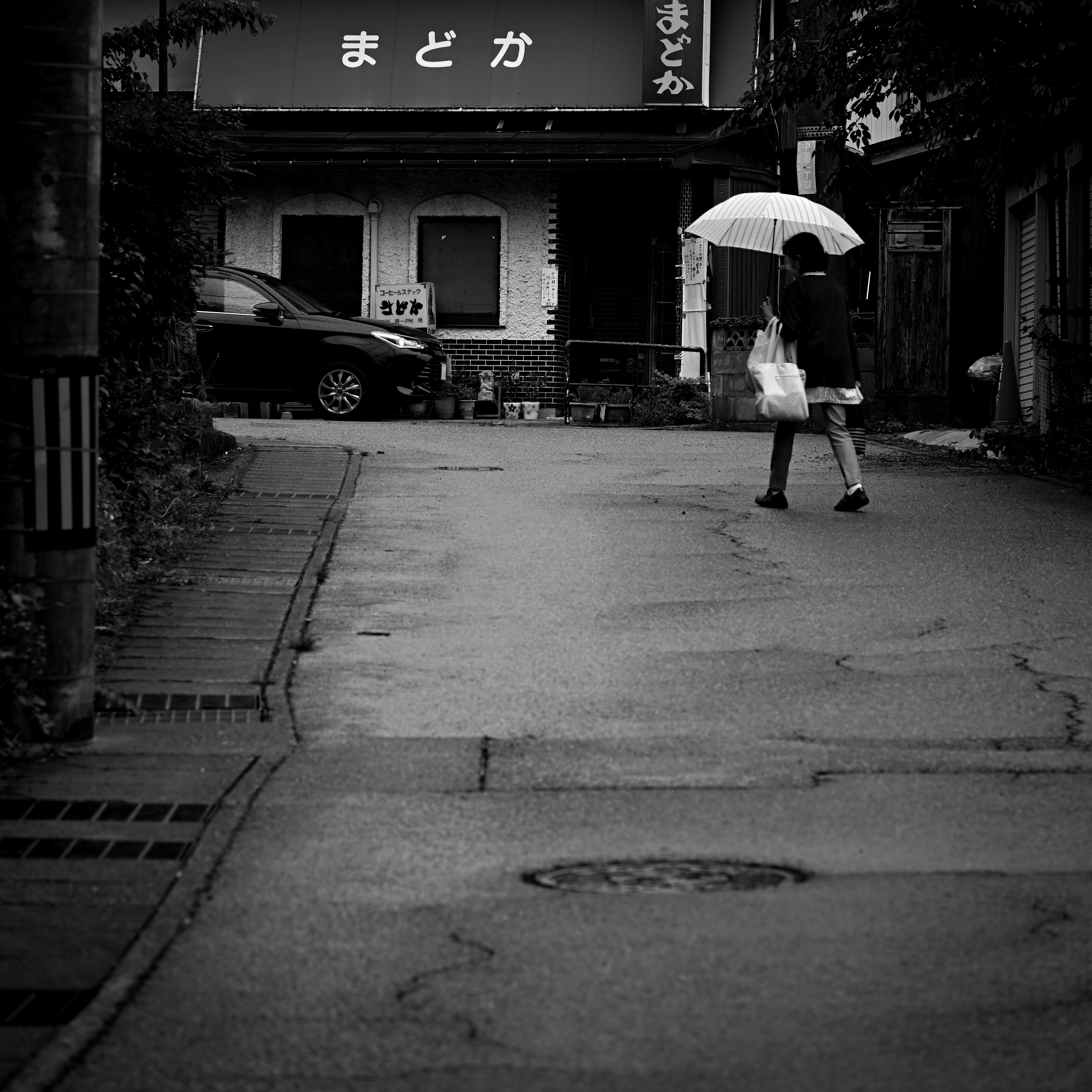 雨の路地で傘をさす人と奥行きのある街並み