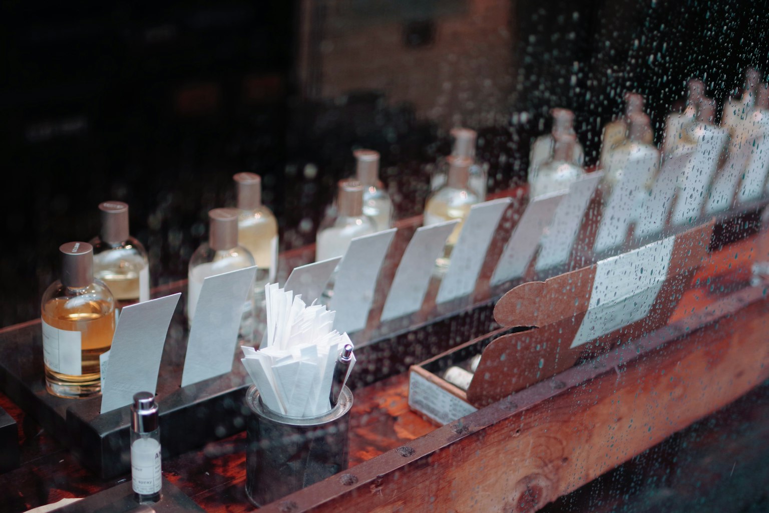 View of perfume bottles lined up in a store through rain-soaked glass
