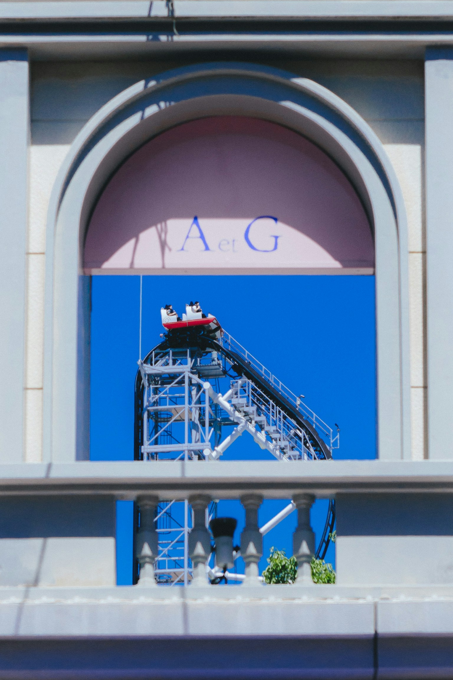 Jendela busur bangunan dengan roller coaster terlihat melawan langit biru