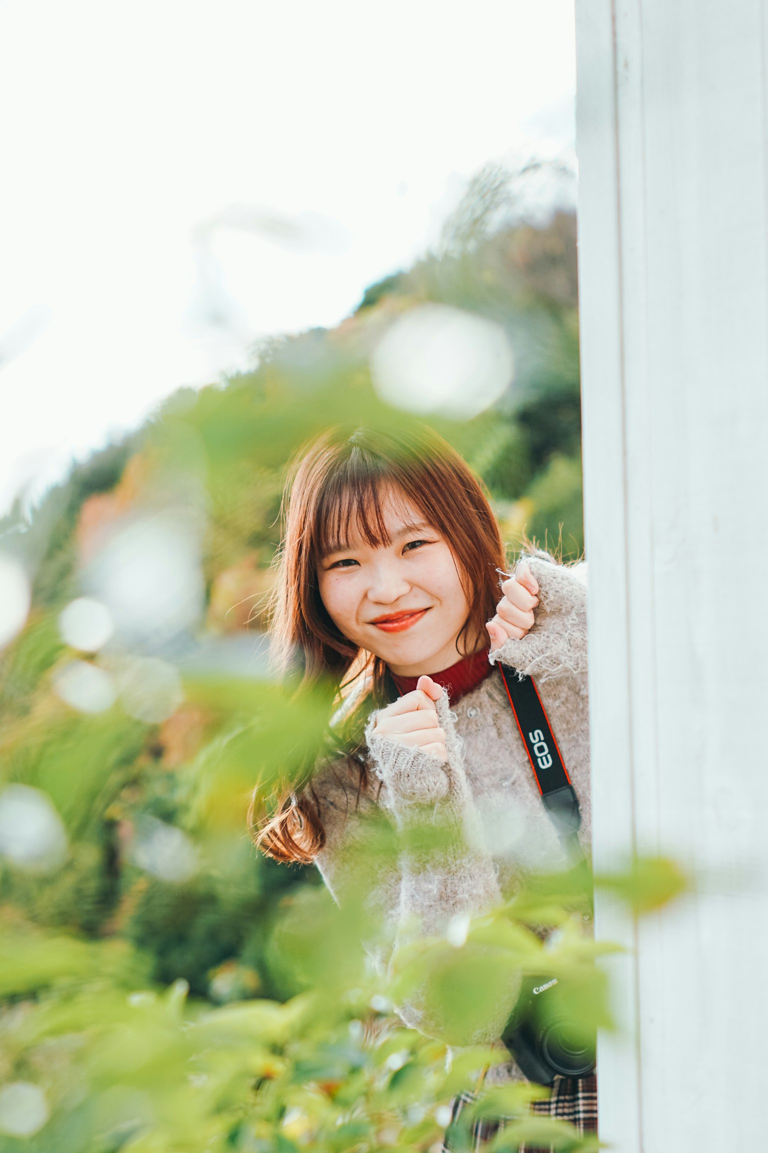 緑の葉の間から顔を出す女性 笑顔で親指を立てている 自然の中での楽しい瞬間