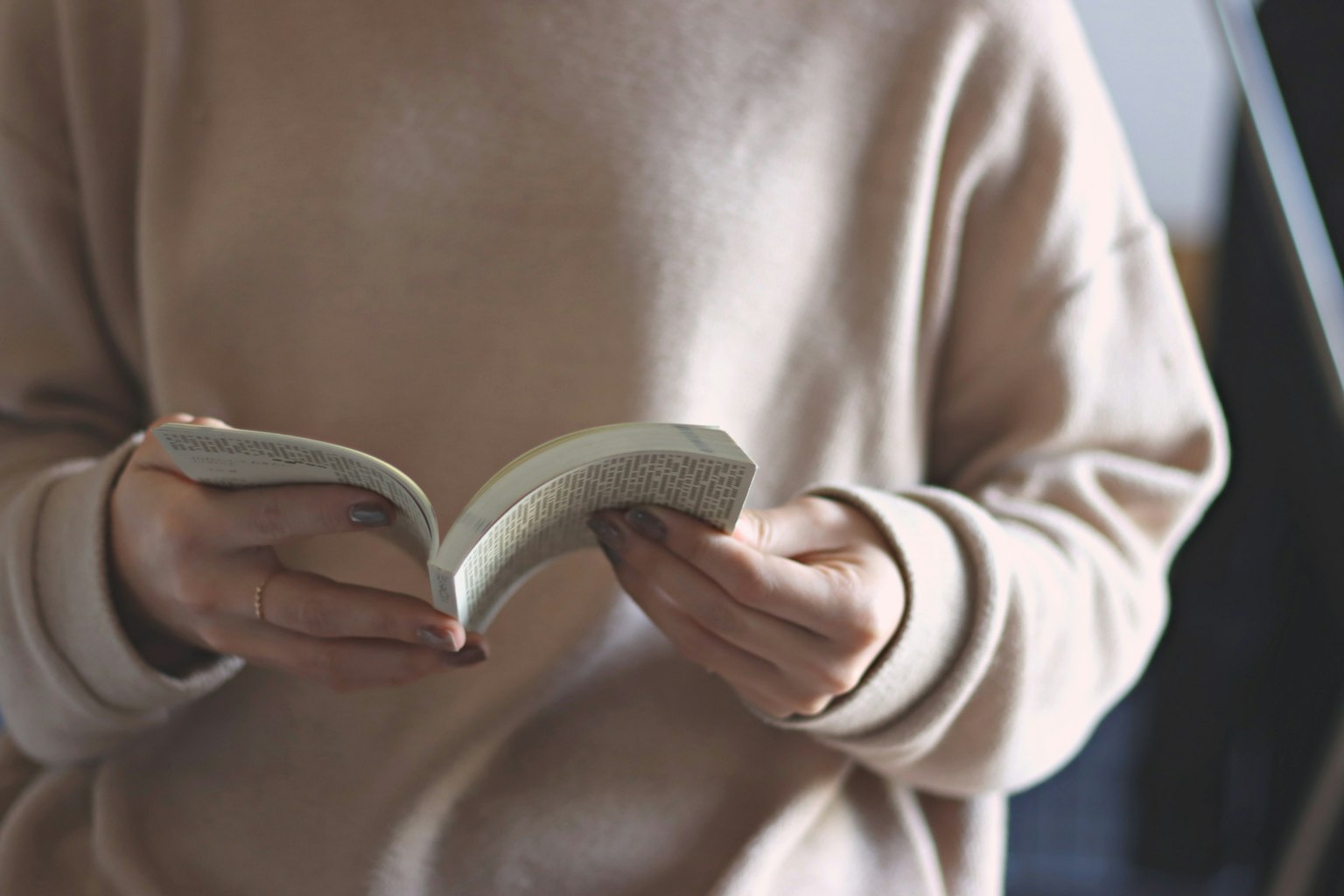 Person holding a book while wearing a soft-colored sweater