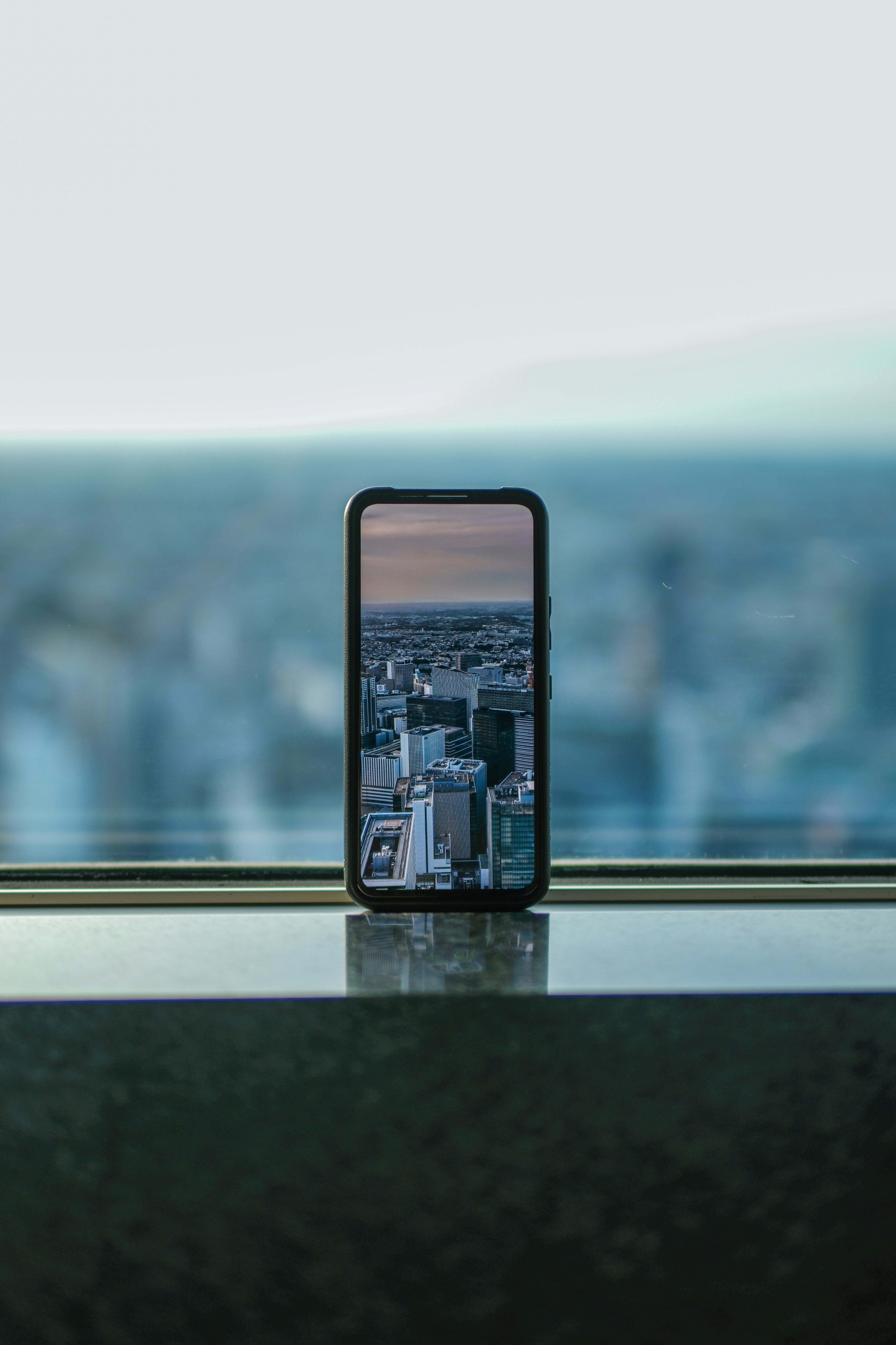 窓辺に置かれたスマホ越しの都市の眺め