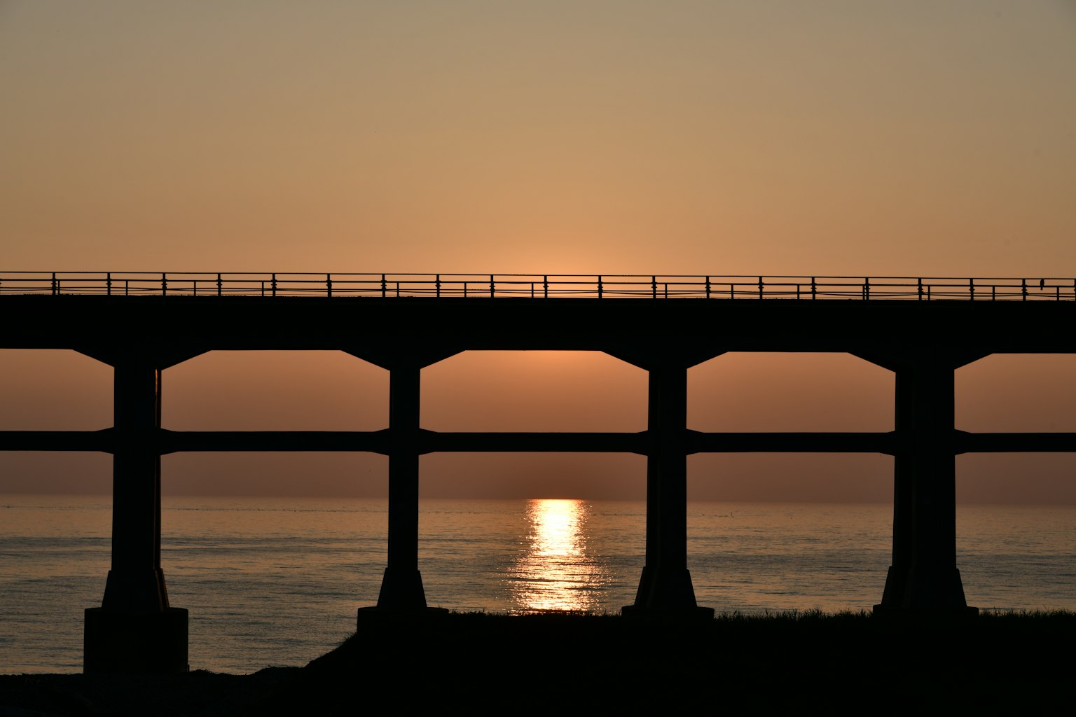 Silueta de un puente contra un atardecer reflejado en el mar