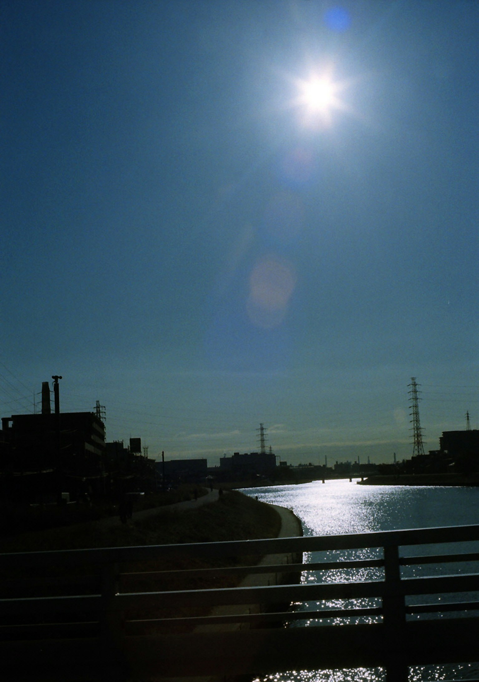 Sole che brilla su un fiume con uno sfondo industriale che include fabbriche e linee elettriche