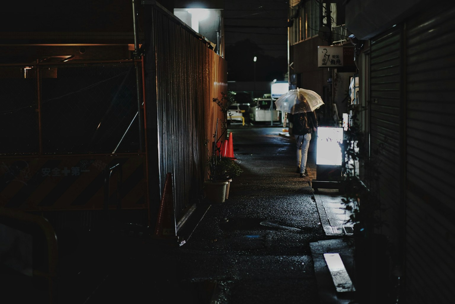 A figure standing in a dark alley illuminated by streetlights