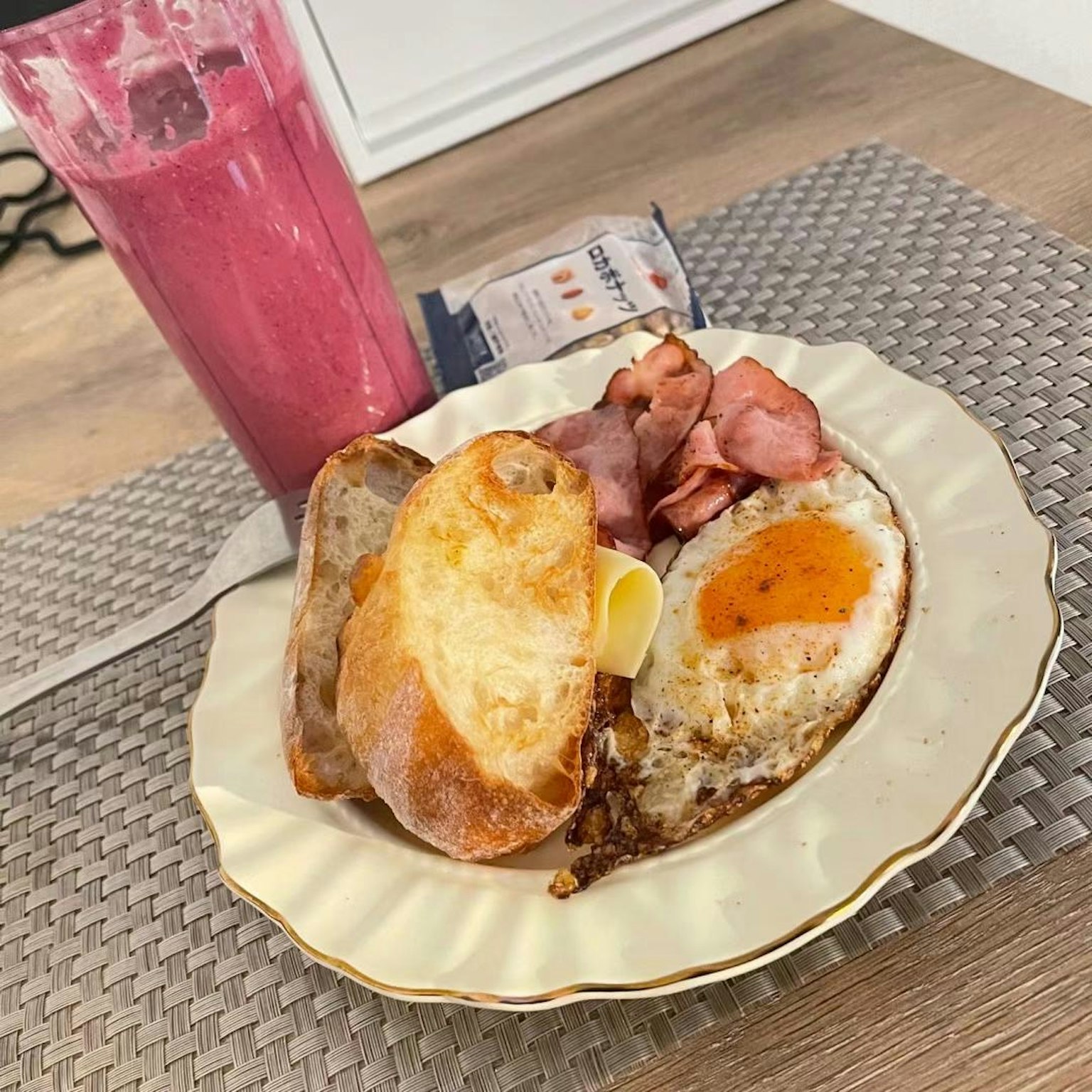 Piring sarapan dengan telur goreng ham dan roti bakar disajikan dengan smoothie merah muda