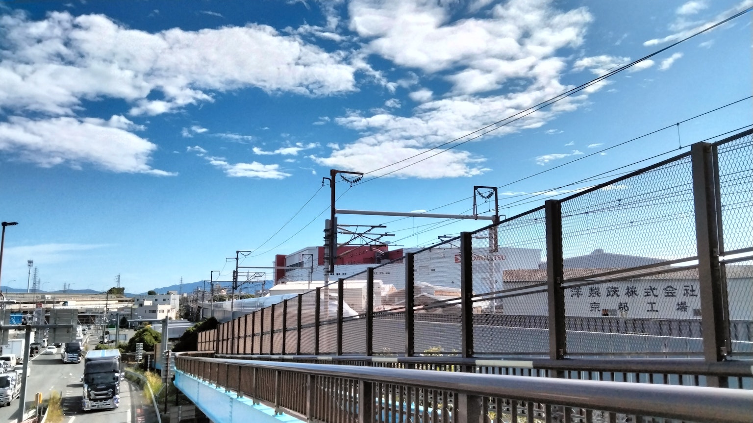 Paisaje con cielo azul y nubes blancas que presenta ferrocarriles y edificios