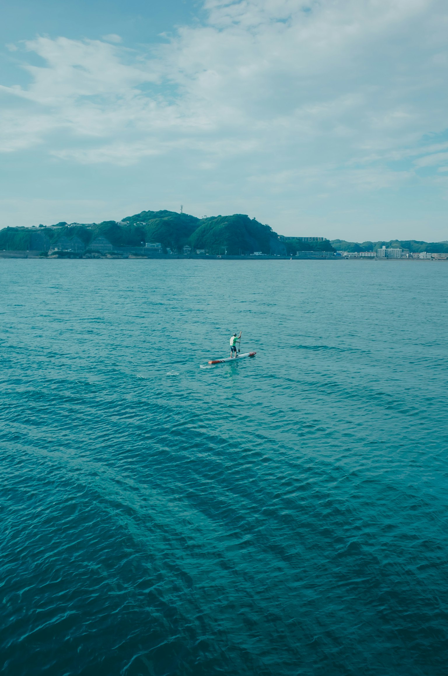 Une personne faisant du kayak sur une mer bleue avec un ciel calme et des collines au loin