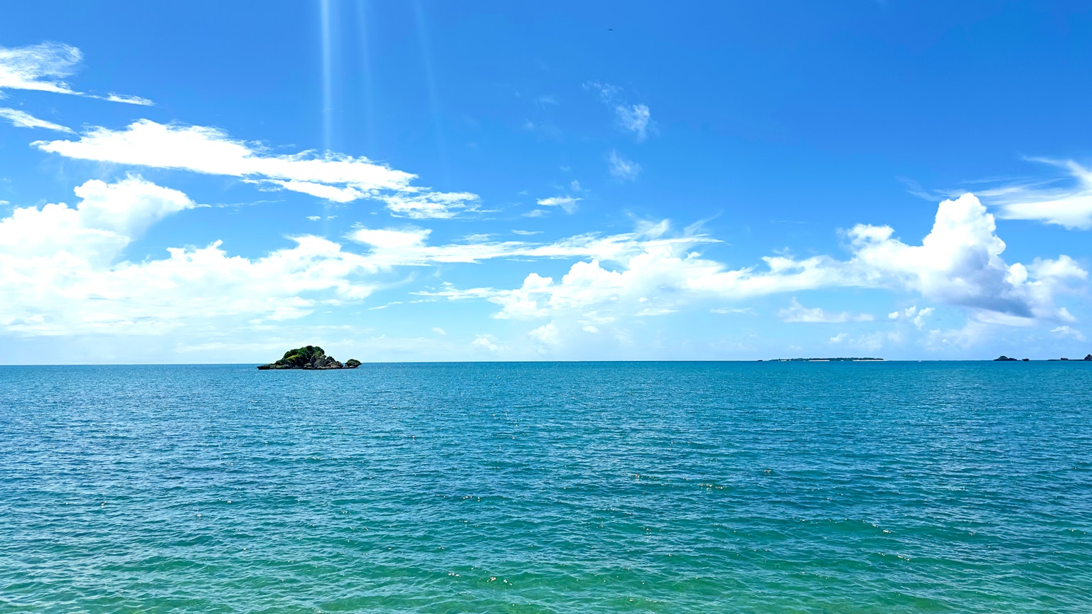 Eine malerische Aussicht auf den blauen Ozean und den Himmel mit einer kleinen Insel in der Ferne