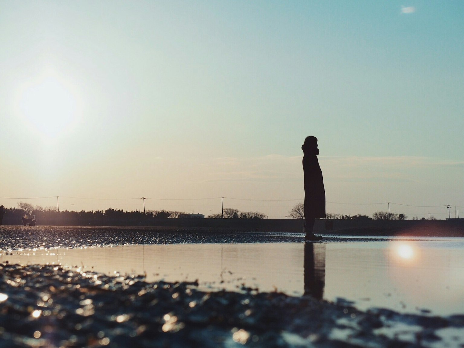 Una persona in piedi vicino all'acqua al tramonto con riflessi