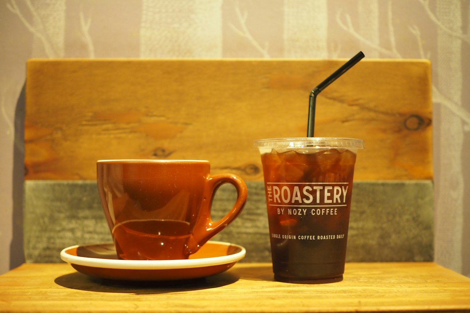 ถ้วยกาแฟสีน้ำตาลและถ้วยกาแฟเย็นบนโต๊ะไม้