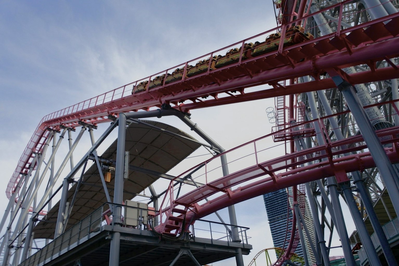 Red roller coaster track elevated above a structure with blue sky in the background