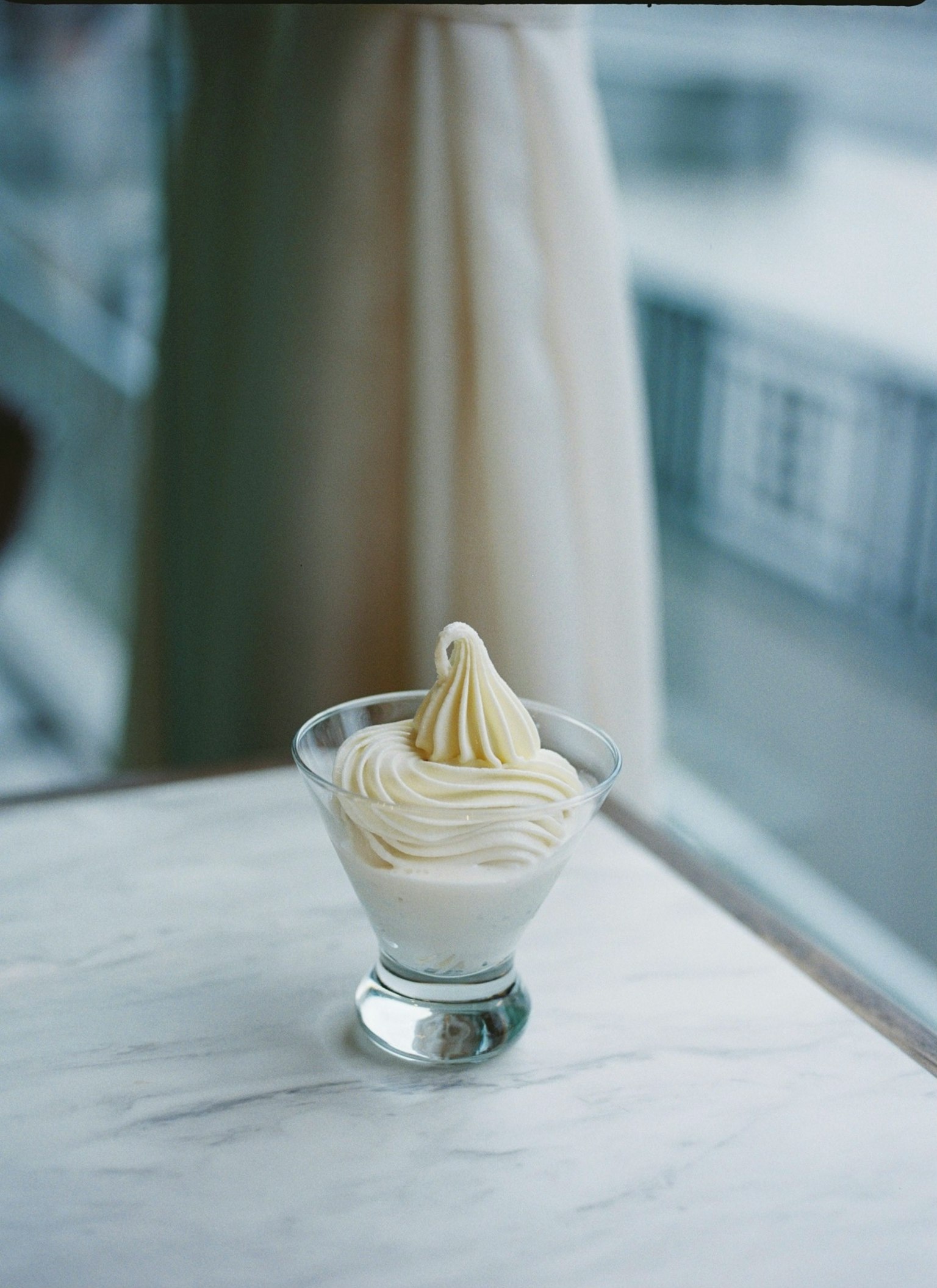 A dessert cup with white cream is placed on a table by the window