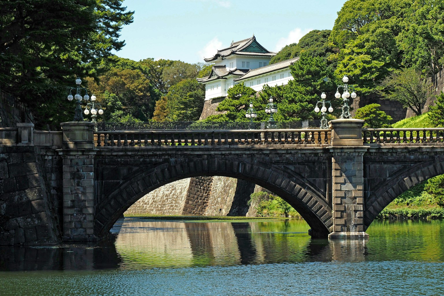 Stone bridge of the Imperial Palace with lush greenery and calm water