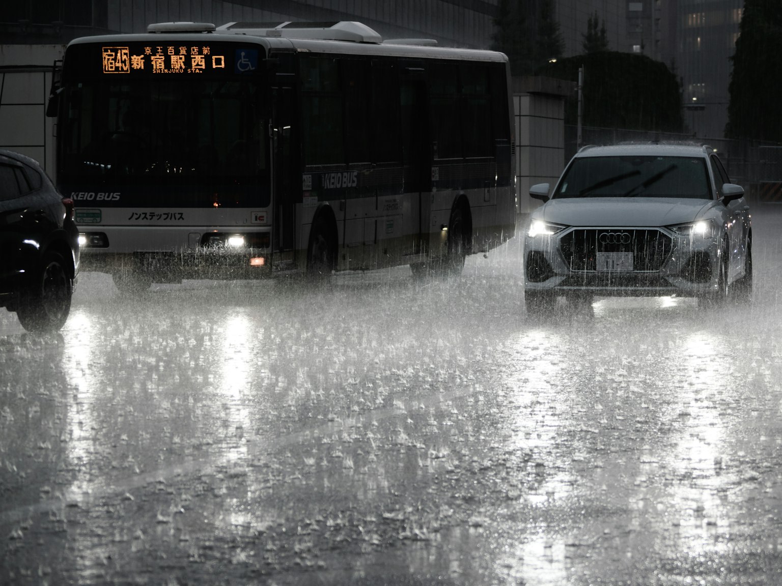 大雨中巴士與汽車行駛的場景，水洼形成