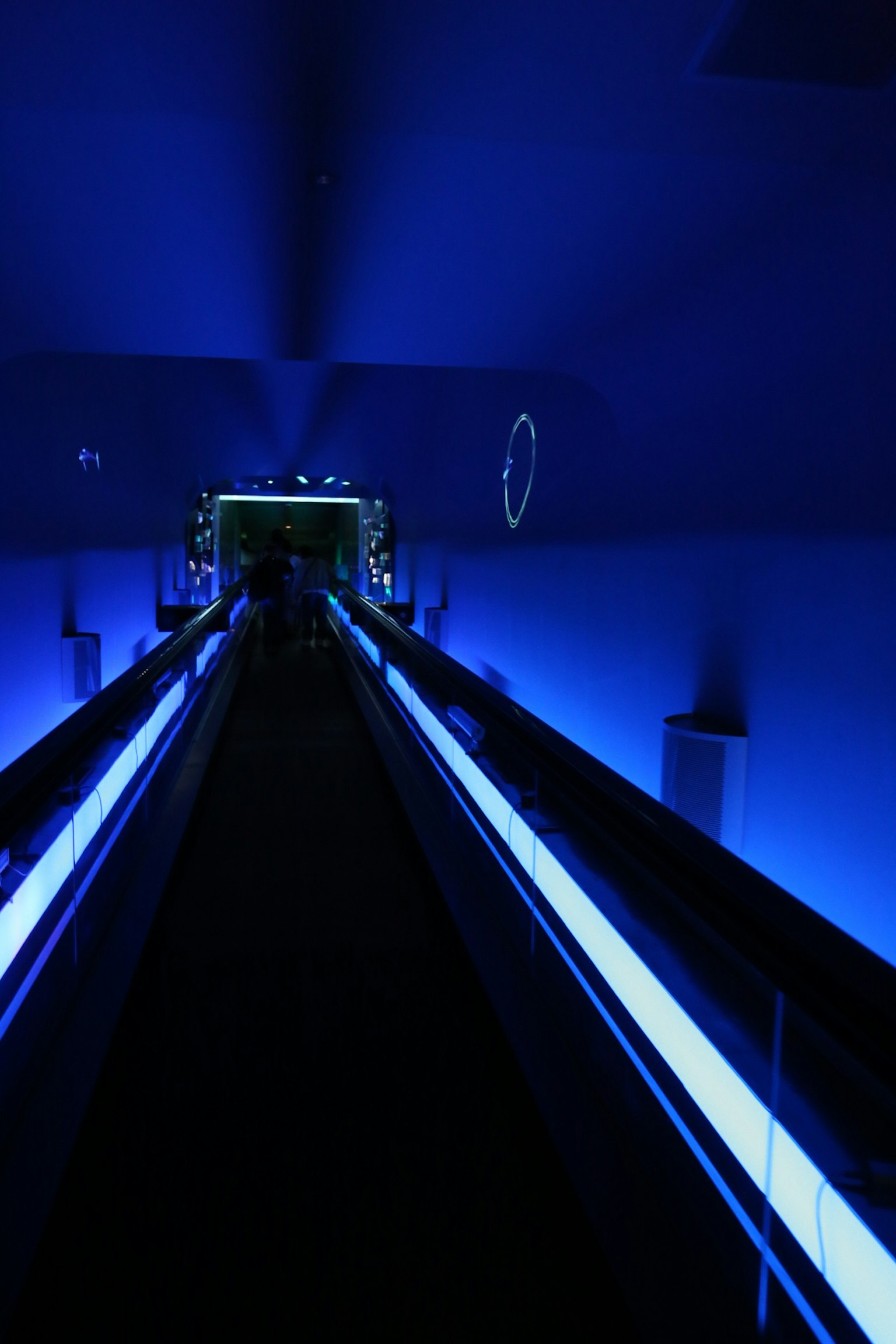 Long corridor illuminated by blue lights with a moving walkway