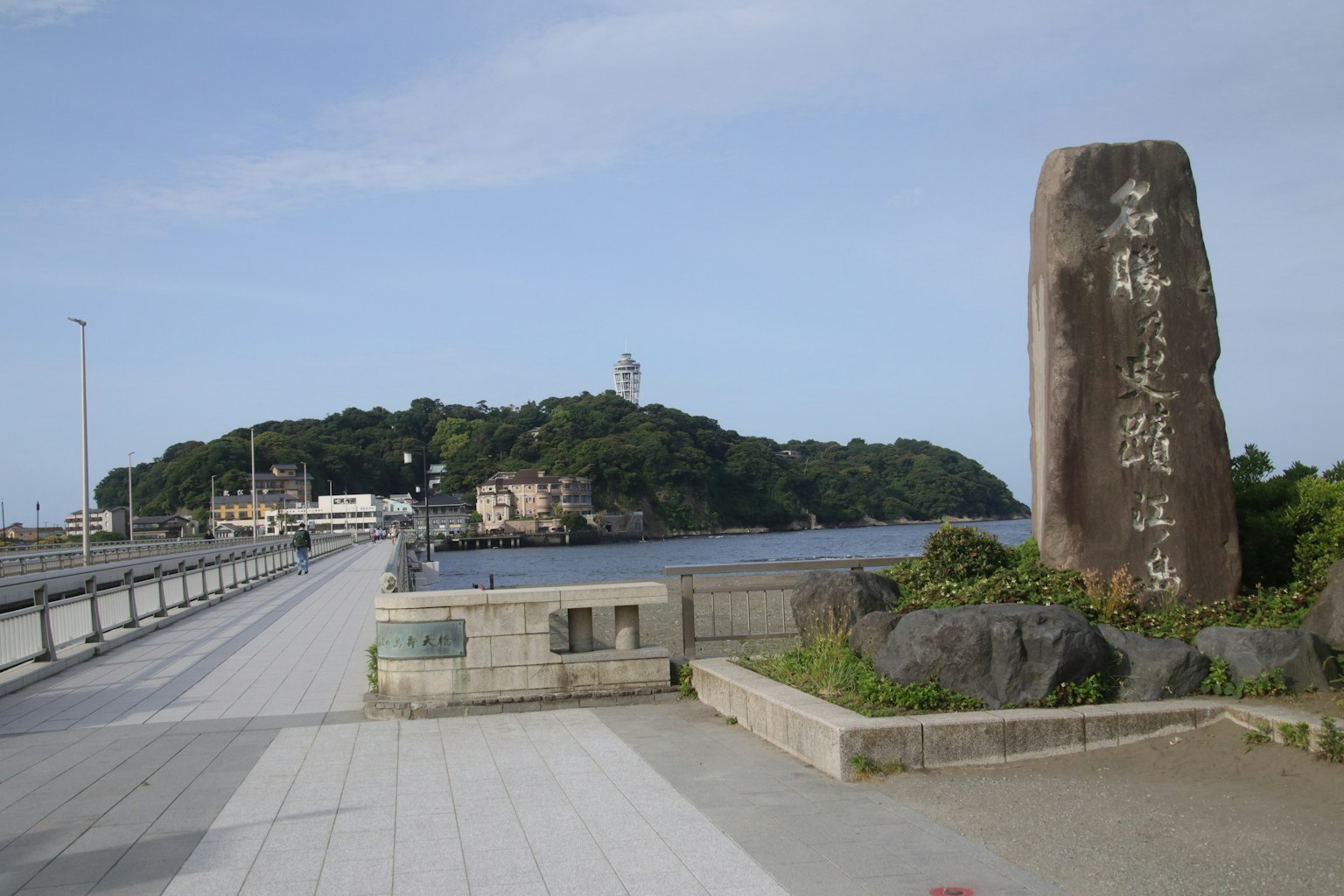 Pemandangan pantai dengan monumen dan pulau serta mercusuar di kejauhan