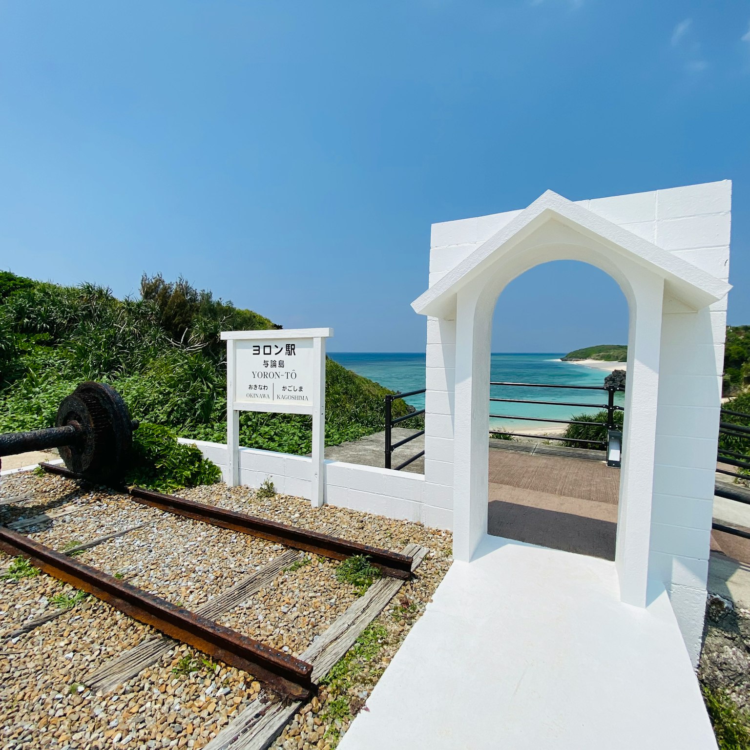 Arco bianco che conduce alla spiaggia con binari