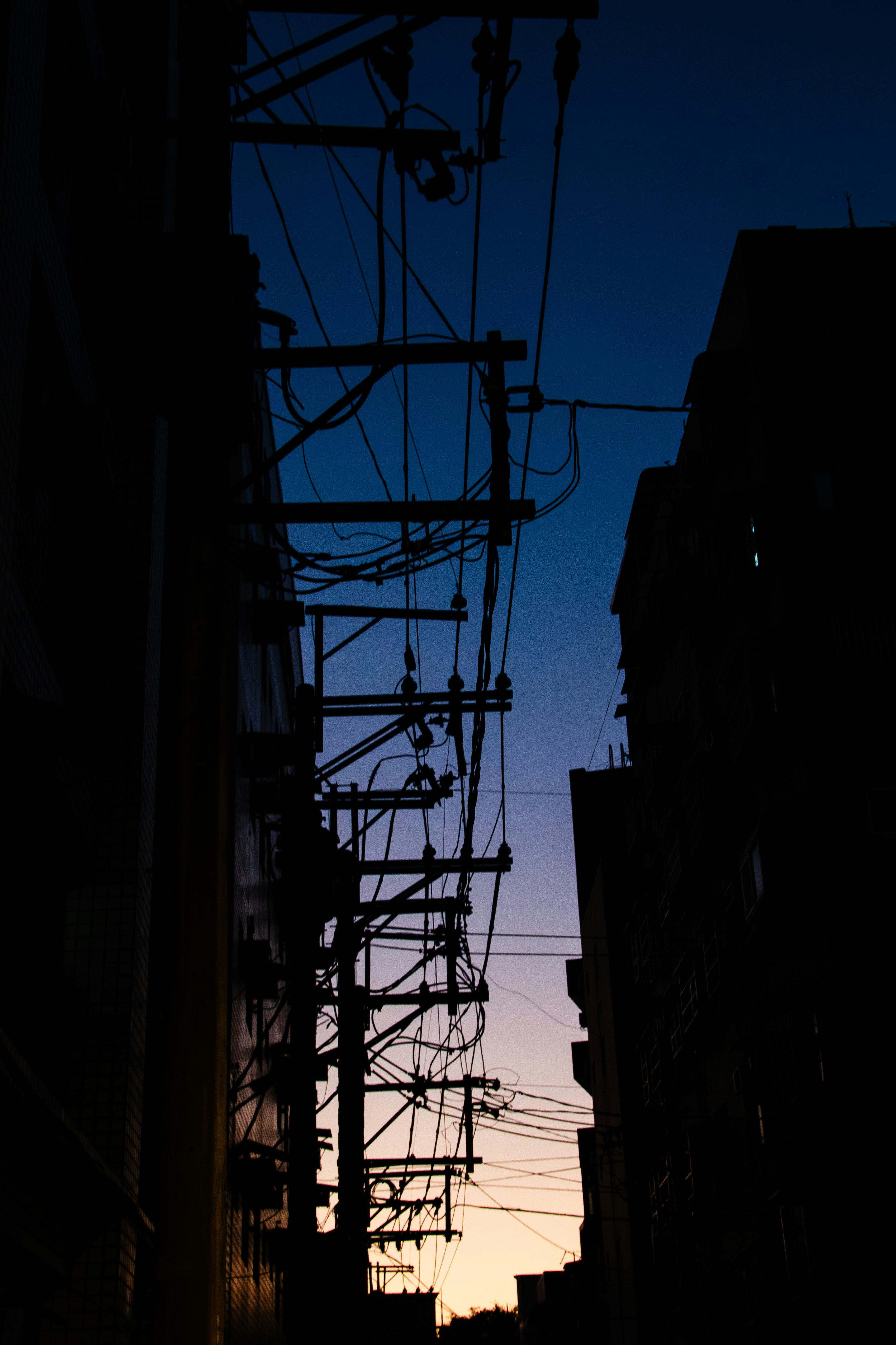 夕暮れの路地に並ぶ電線と街灯のシルエット