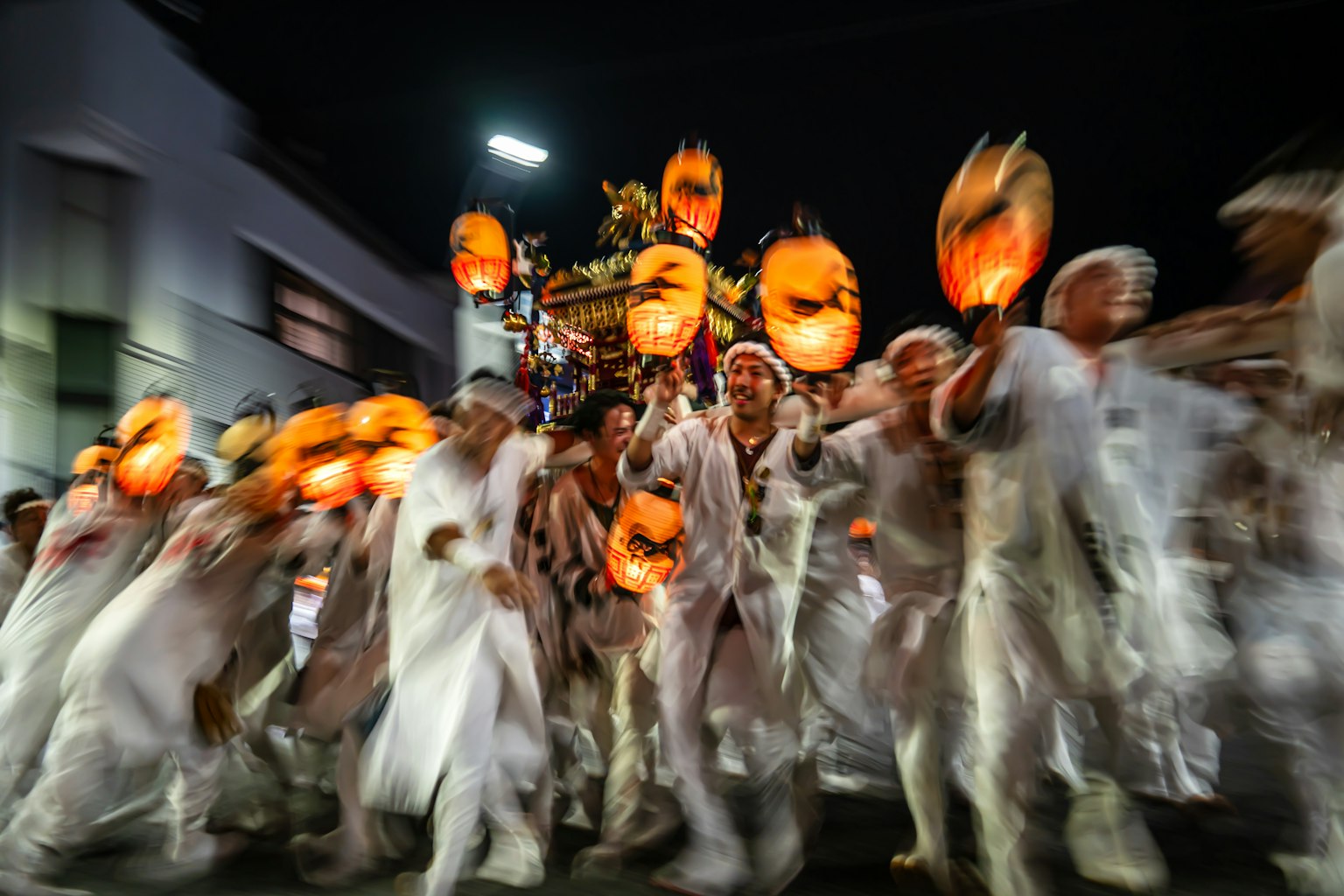 Menschen in weißen Kostümen halten orangefarbene Laternen während eines Nachtfestes