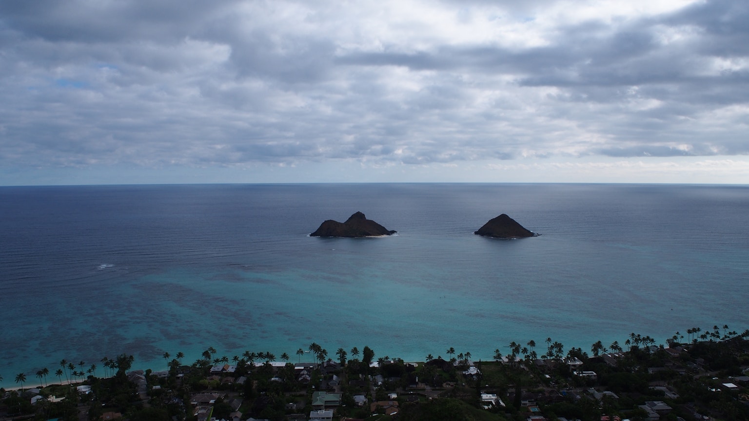Scenic view of two small islands in a blue ocean under a cloudy sky