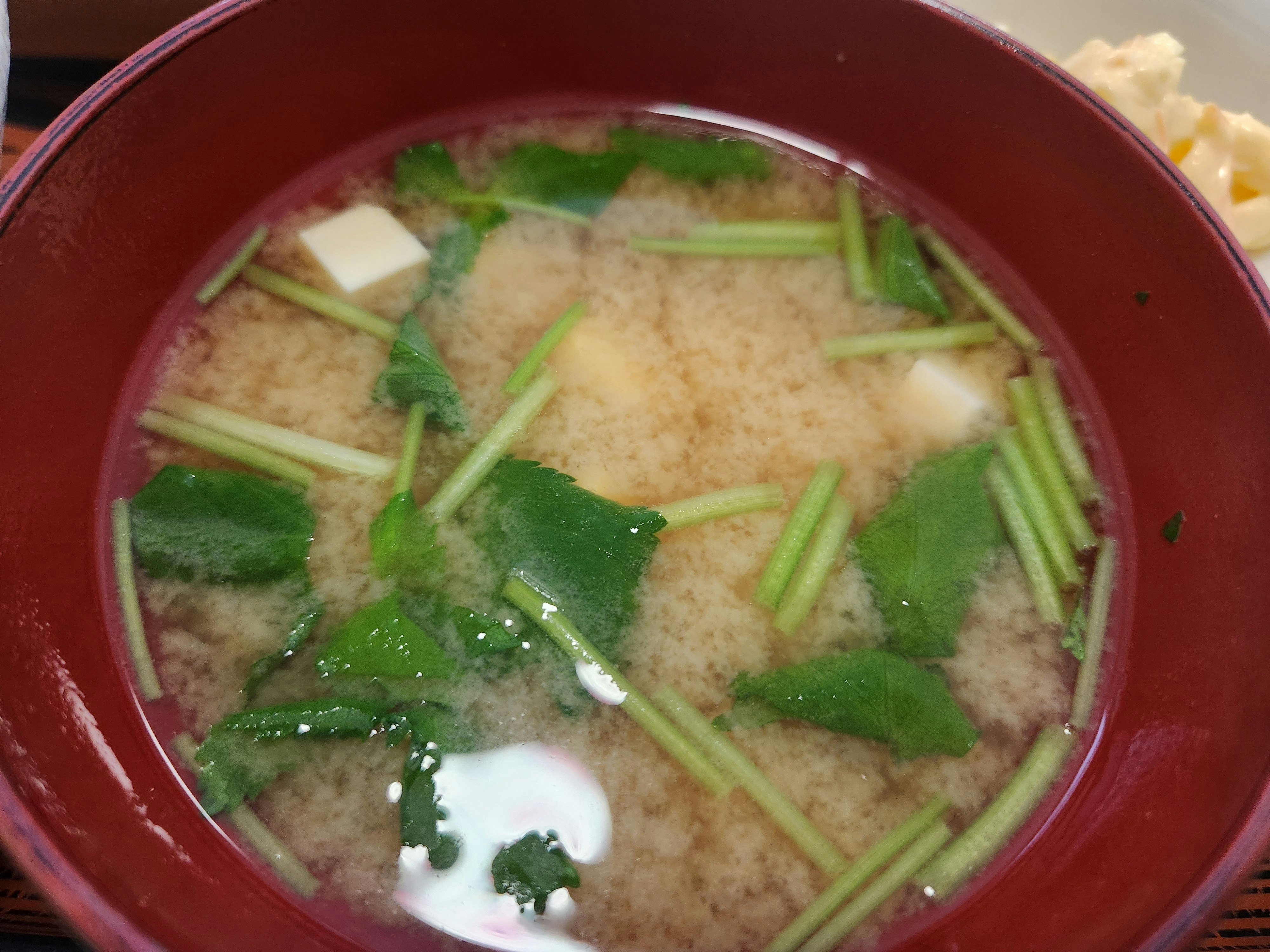 赤い器に入った味噌汁 豆腐と野菜が浮かんでいる