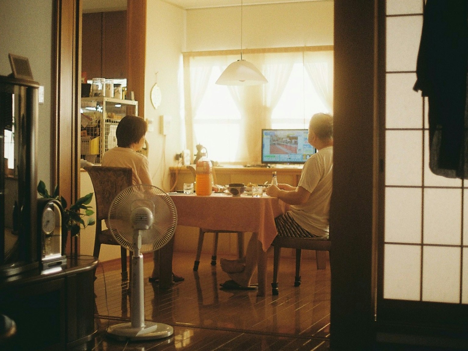 二人がテーブルに座っている部屋の内部の風景 窓からの自然光が差し込み テーブルには飲み物とコンピュータがある