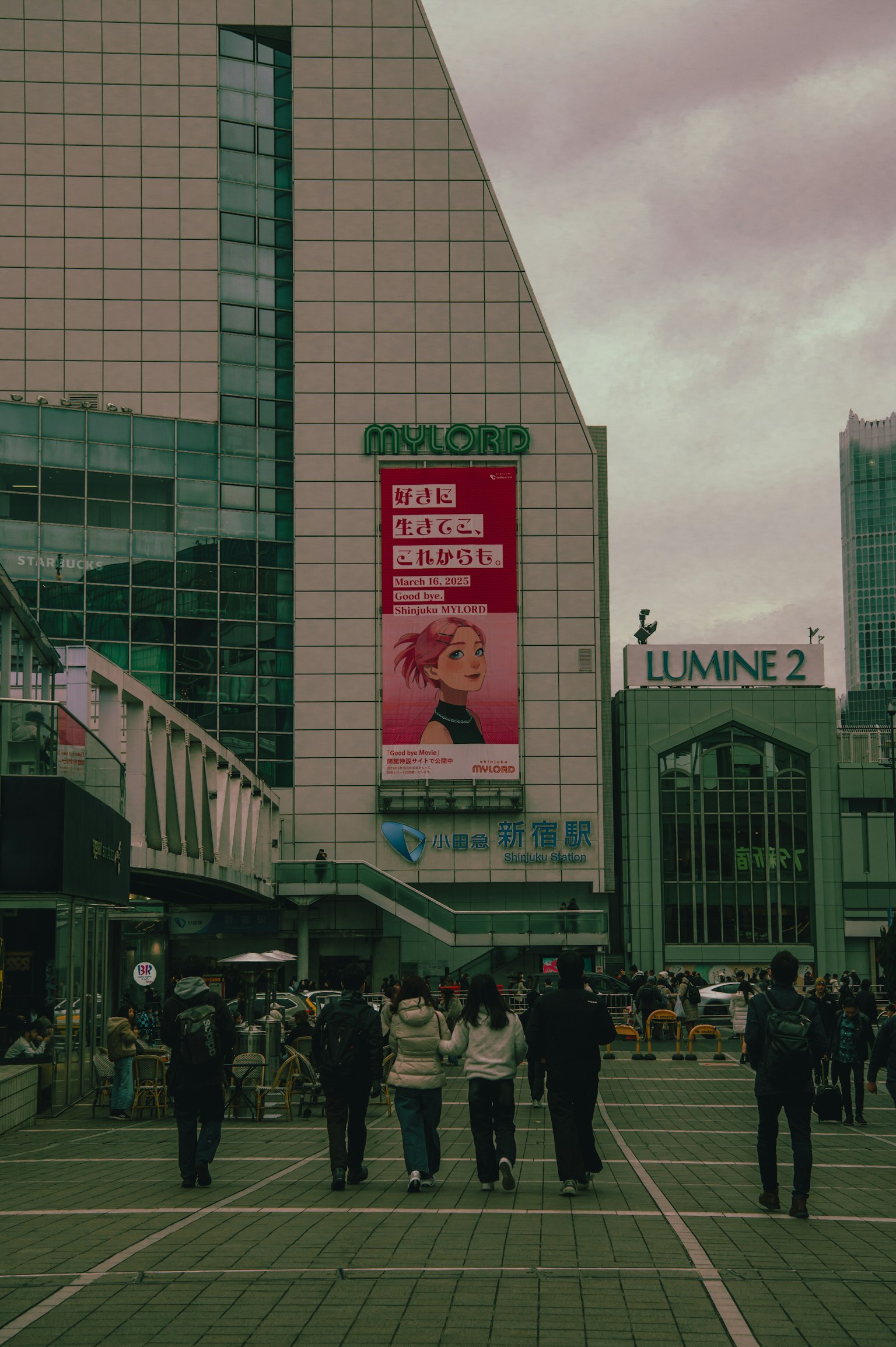Crowd of people in a lively urban square with a large advertisement