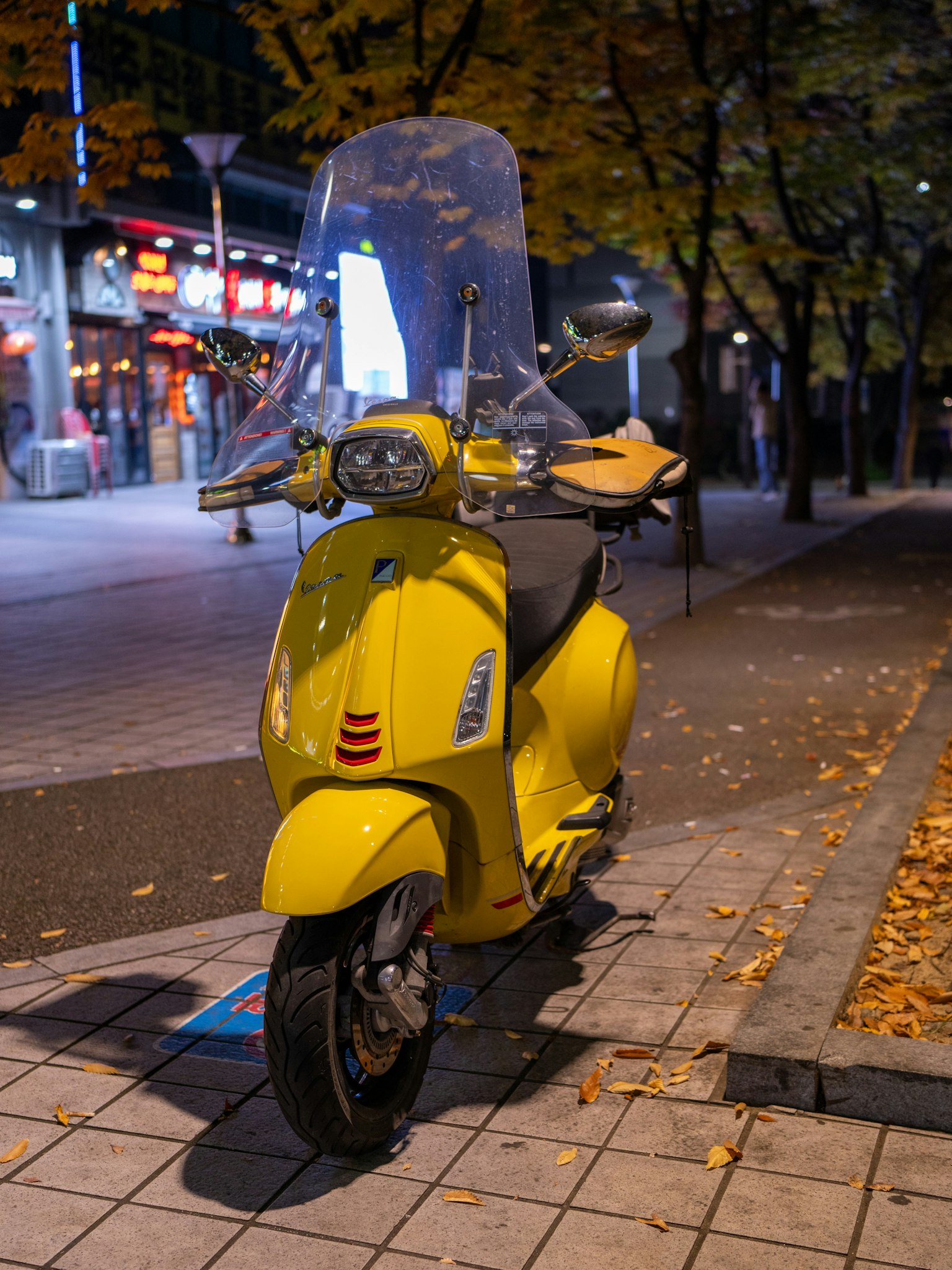 夜の街に停まっている黄色いスクーターと落ち葉