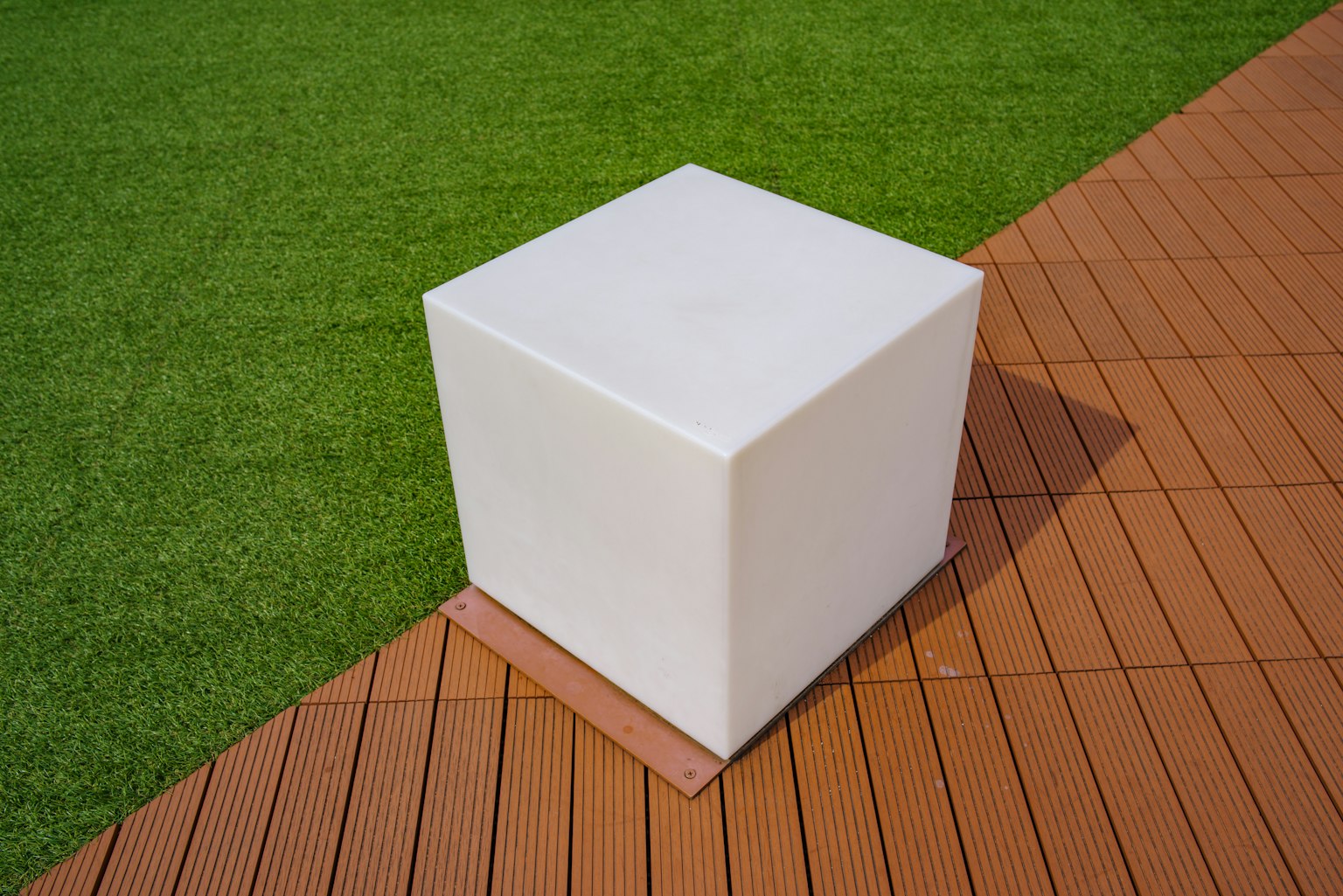 Ein weißer Würfel auf grünem Gras neben einem Holzdeck platziert