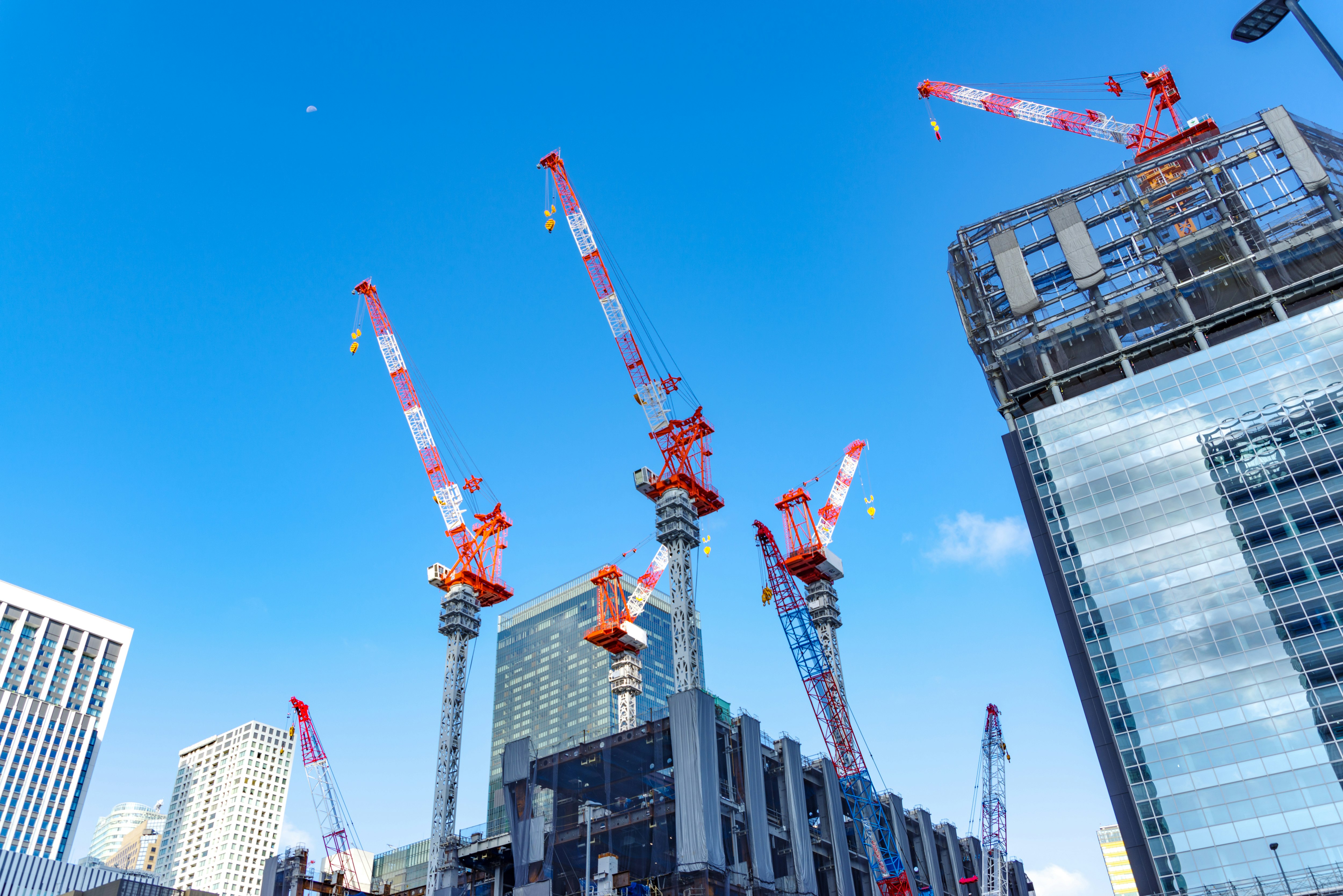 grúas alineadas en un sitio de construcción de gran altura bajo un cielo azul