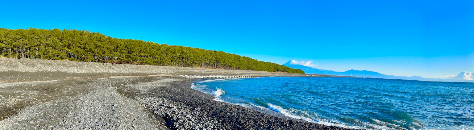 Pemandangan panorama pantai dengan langit dan laut biru Kerikil tersebar di sepanjang pantai Pohon hijau di latar belakang