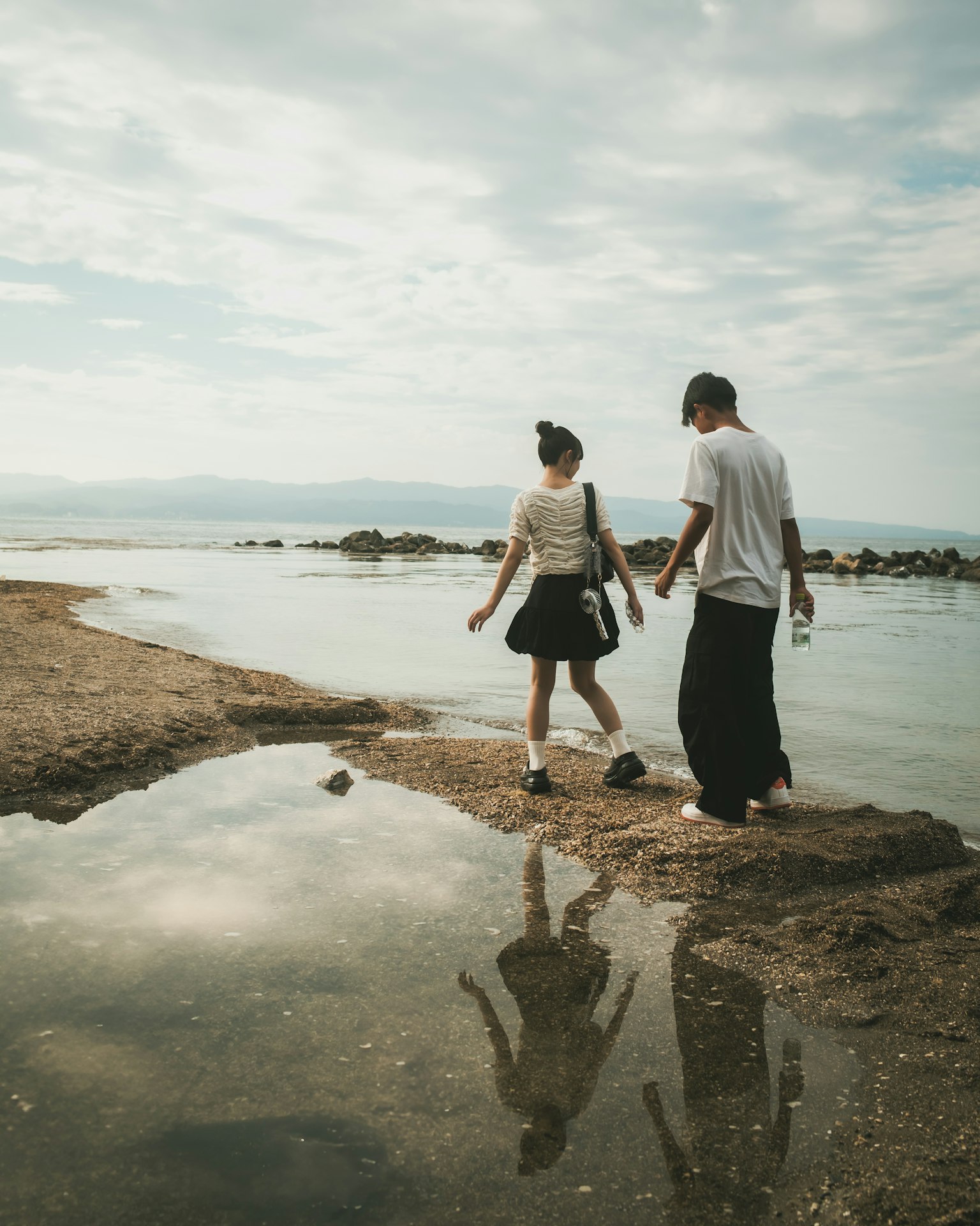 カップルが水辺を歩いている風景 反射が美しい穏やかな海