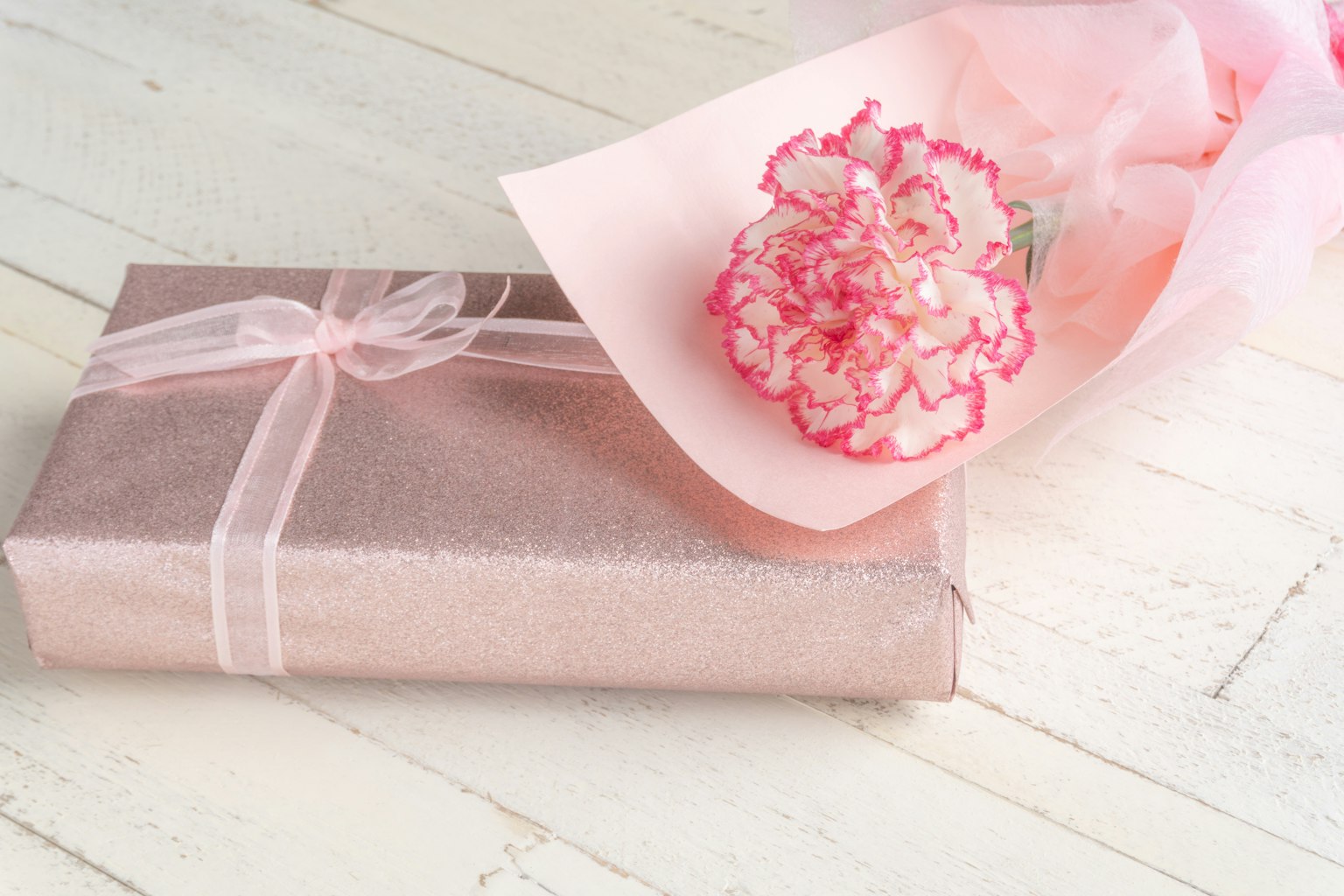 ของขวัญที่ห่อด้วยสีชมพูพร้อมช่อการ์เนชั่น