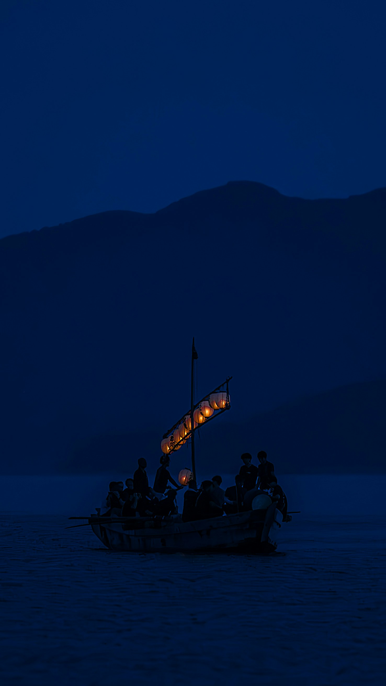 群青の海上で灯りを浮かべる舟と人々の宵の祭風景