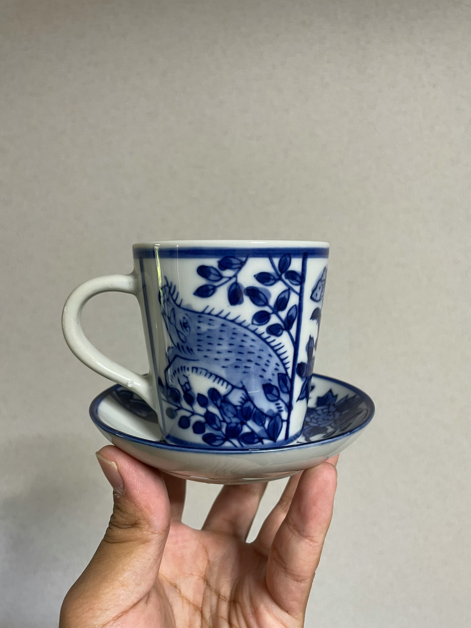Hand hält eine blaue Porzellantasse mit Blumenmuster und Untertasse