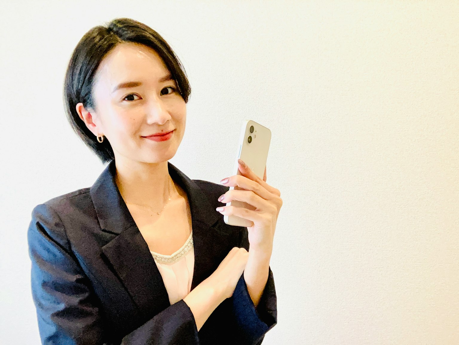 Seorang wanita dalam setelan bisnis tersenyum sambil memegang smartphone