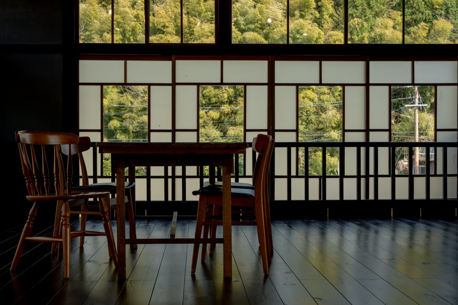 Sebuah ruangan tradisional Jepang dengan meja dan kursi kayu jendela besar yang menampilkan pemandangan hijau