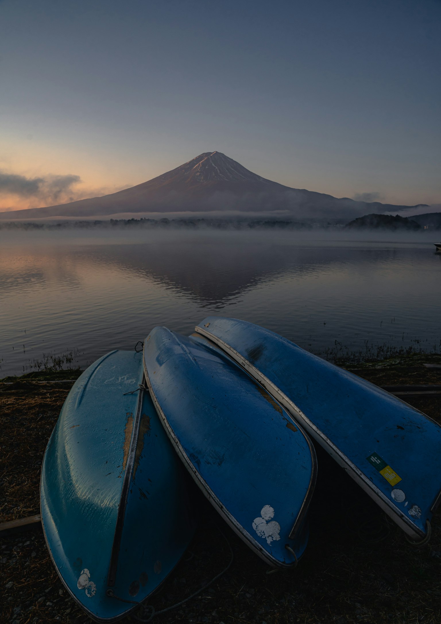 静谧的湖面上蓝色独木舟堆叠，背景是富士山