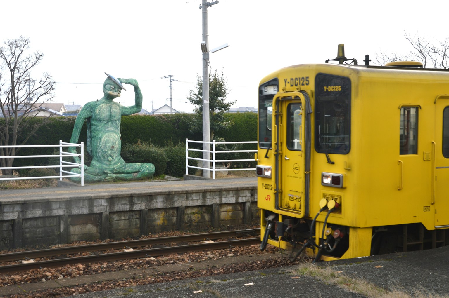 Yellow train beside a bronze statue of a seated figure