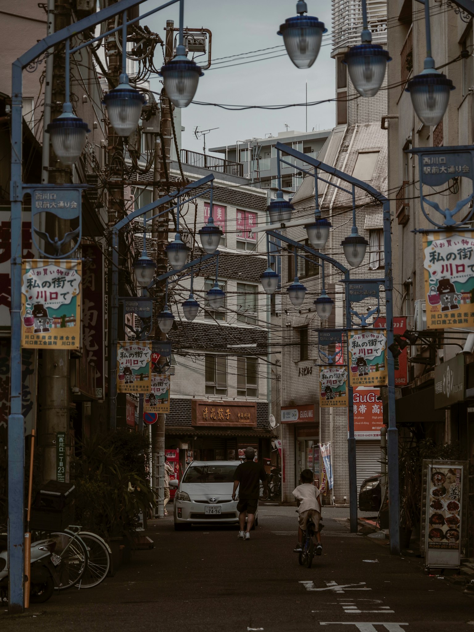 狭い通りに青い街灯と色とりどりの看板が並ぶ風景