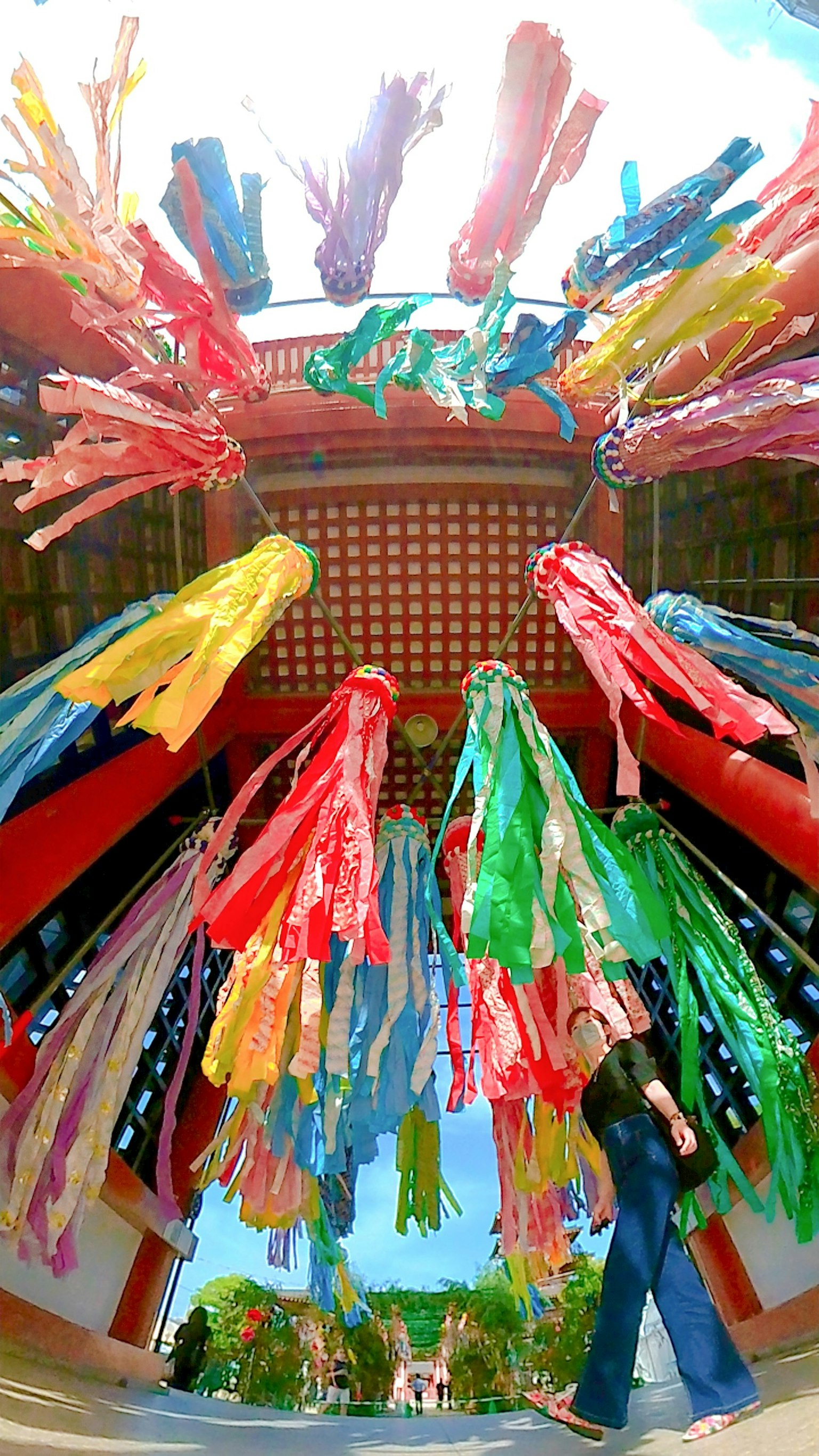 A person standing under a structure adorned with colorful ribbons in a shrine