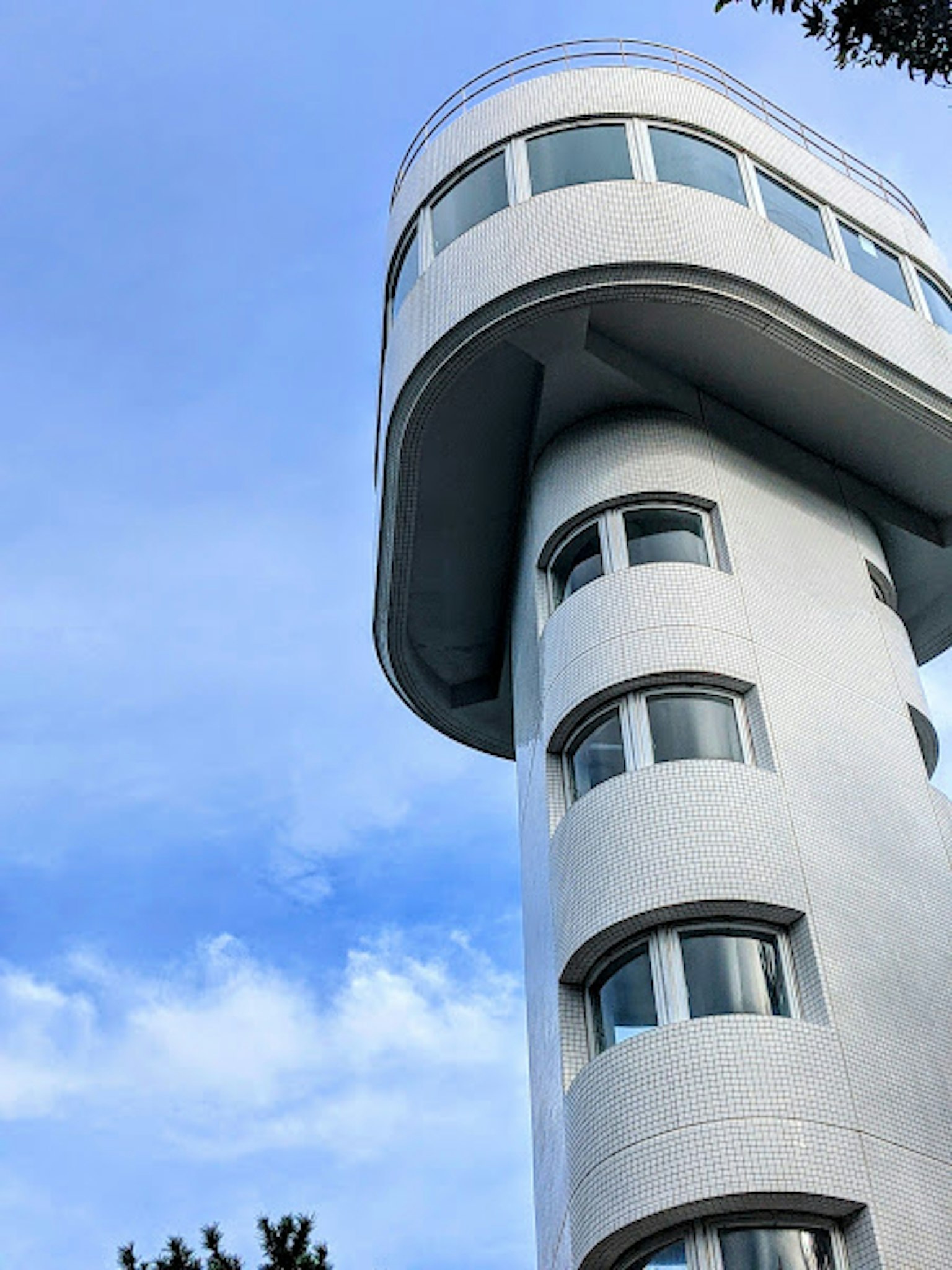 Unique design of a white building topped with a curved structure against a blue sky