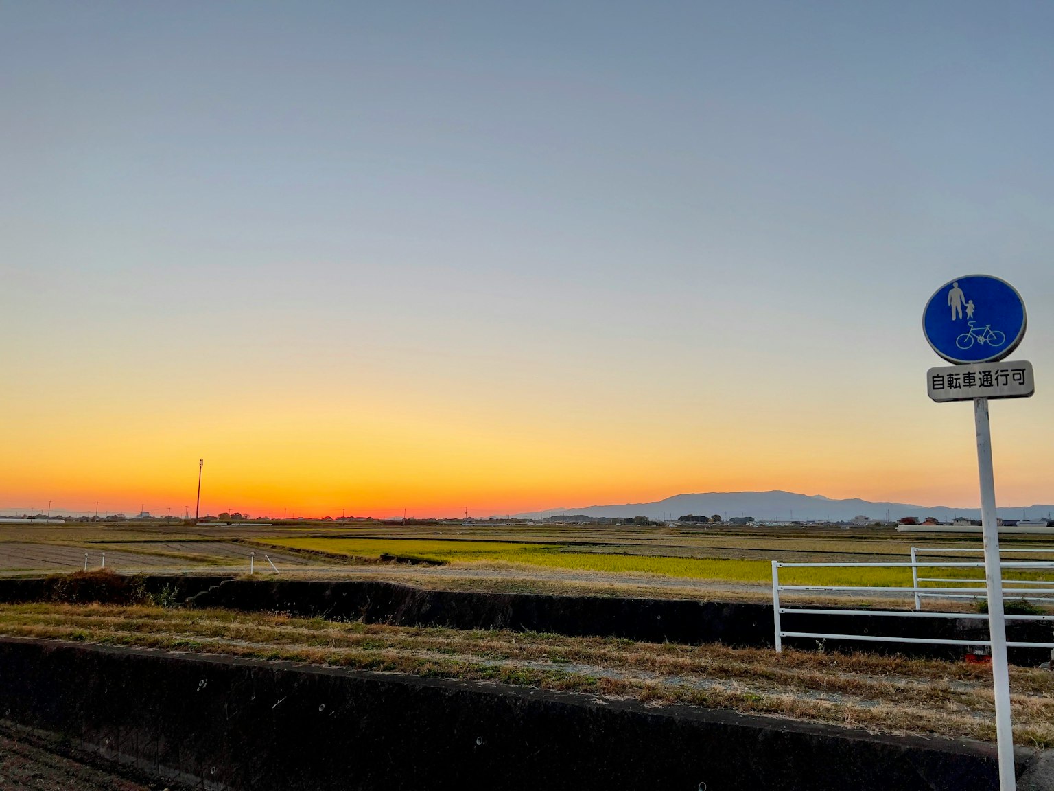A rural landscape with a sunset sky and a pedestrian sign