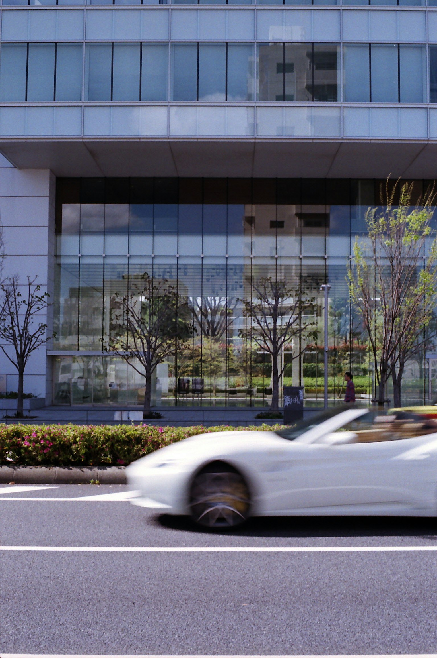 White sports car passing by a modern glass building