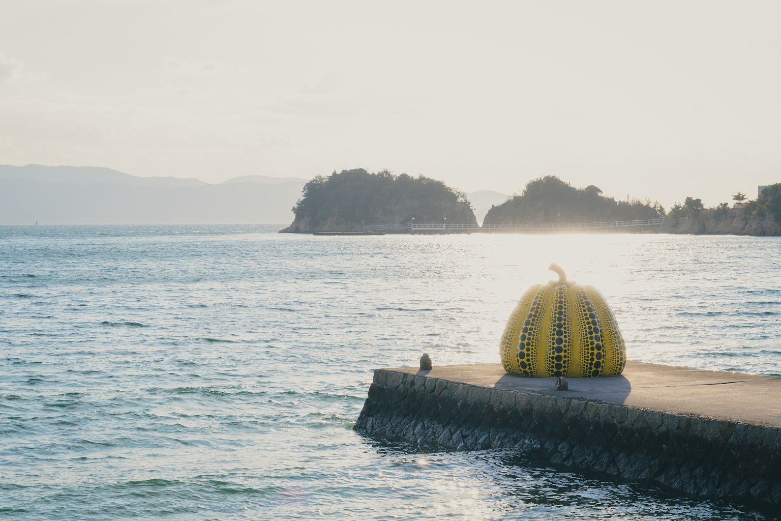 Yellow pumpkin sculpture on a pier with calm sea and distant islands